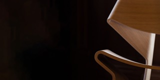 A close up of a brown Scandinavian-style chair on a black background.