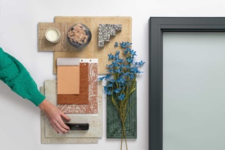 A flat lay with a woman’s hand featuring Gunmetal by Marvin as well as textiles and decor.