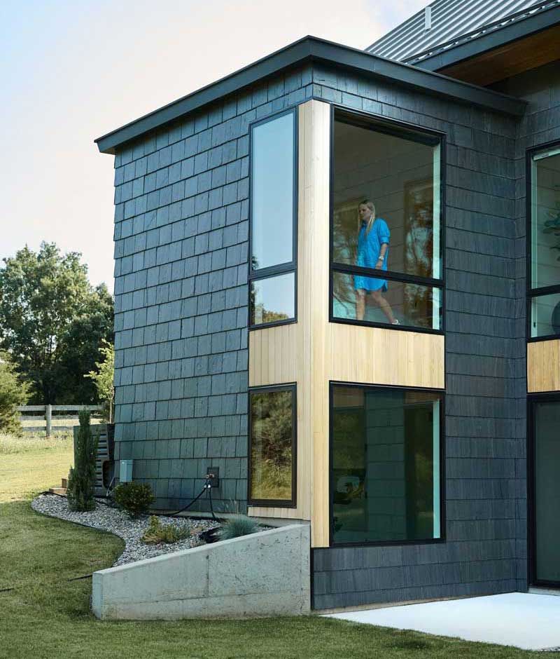 A woman standing inside the second floor of a modern home looking through a Marvin Essential casement window.