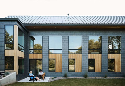 Two people sitting in Adirondack chairs on the patio of a Modern home with Marvin Essential Direct Glaze windows and Essential Casement windows in Ada, Michigan.