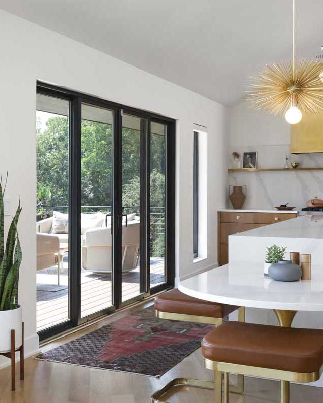 A modern kitchen with white marble island and a Marvin Elevate Sliding Patio door looking out to a deck with patio furniture.