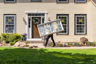 man carrying fiberglass replacement window in front of a house