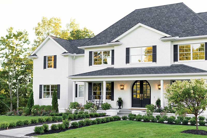 Exterior of a white traditional home with black shutters in New England, featuring Marvin Essential windows and doors.
