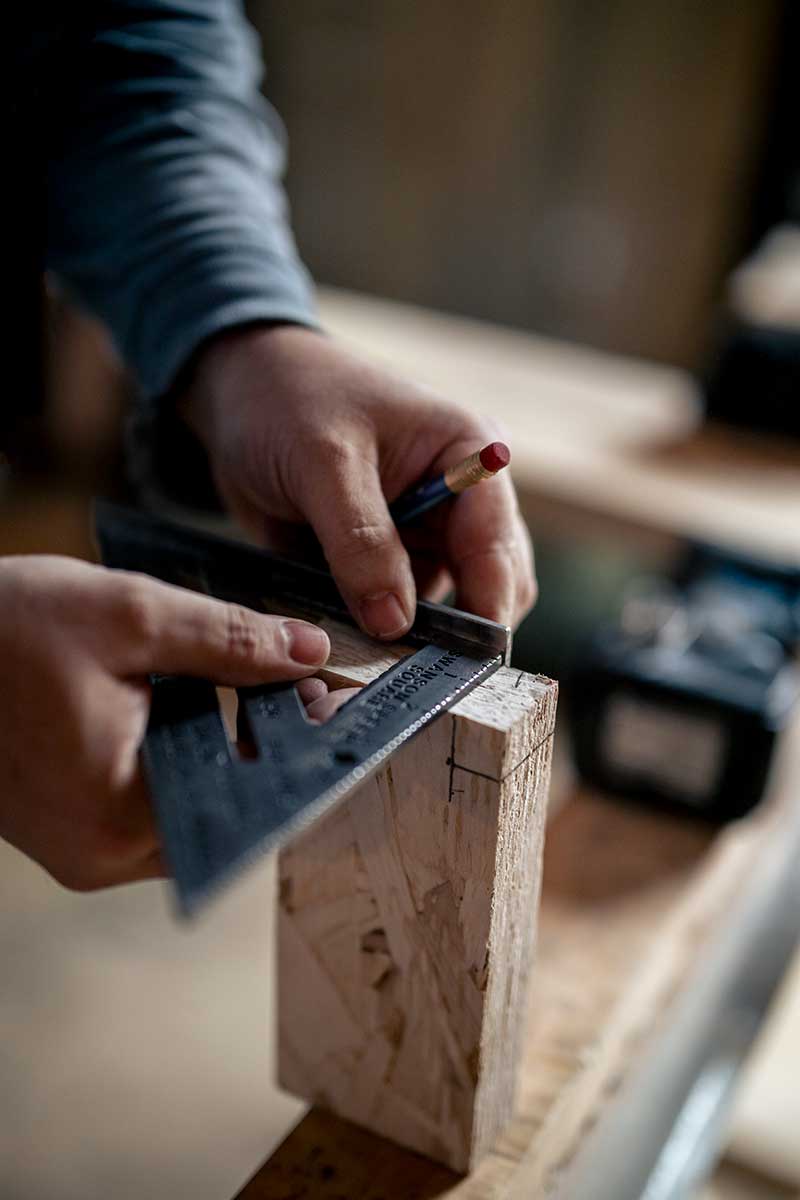 Hands measuring a piece of wood on a job site.