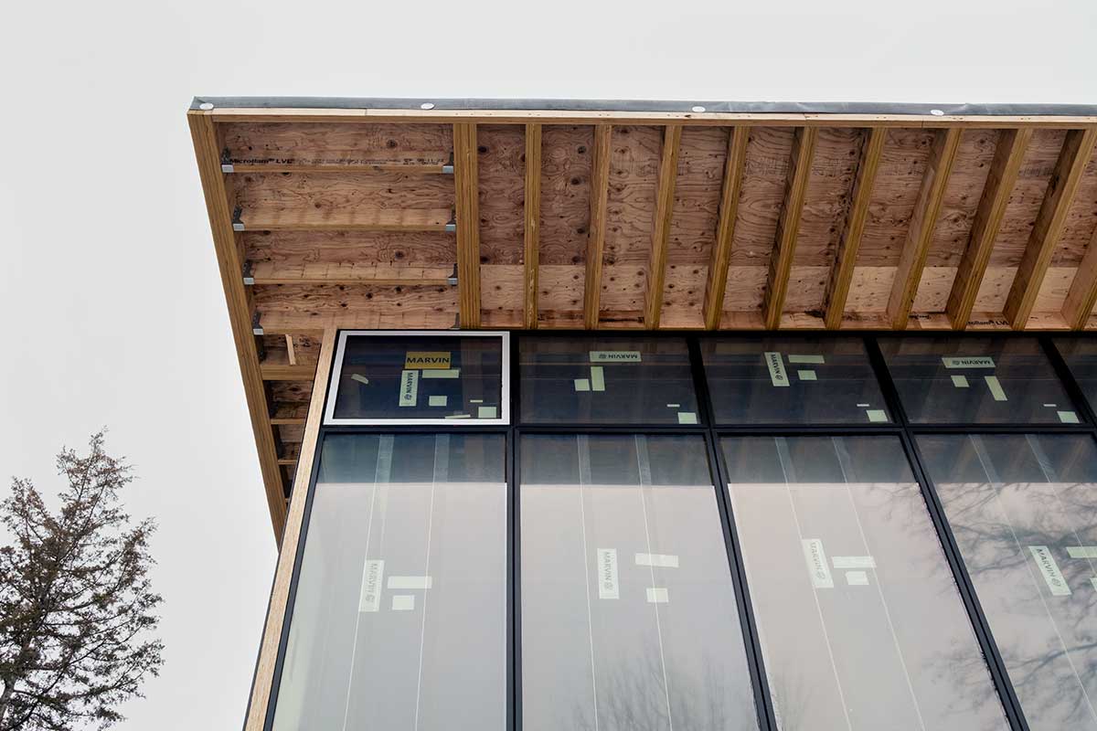 From the ground below, the roof of an under construction home sits above a large wall of Marvin Modern windows.