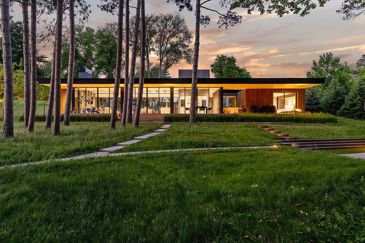 The back of a modern home featuring Marvin Modern windows and doors on a lot with tall trees.