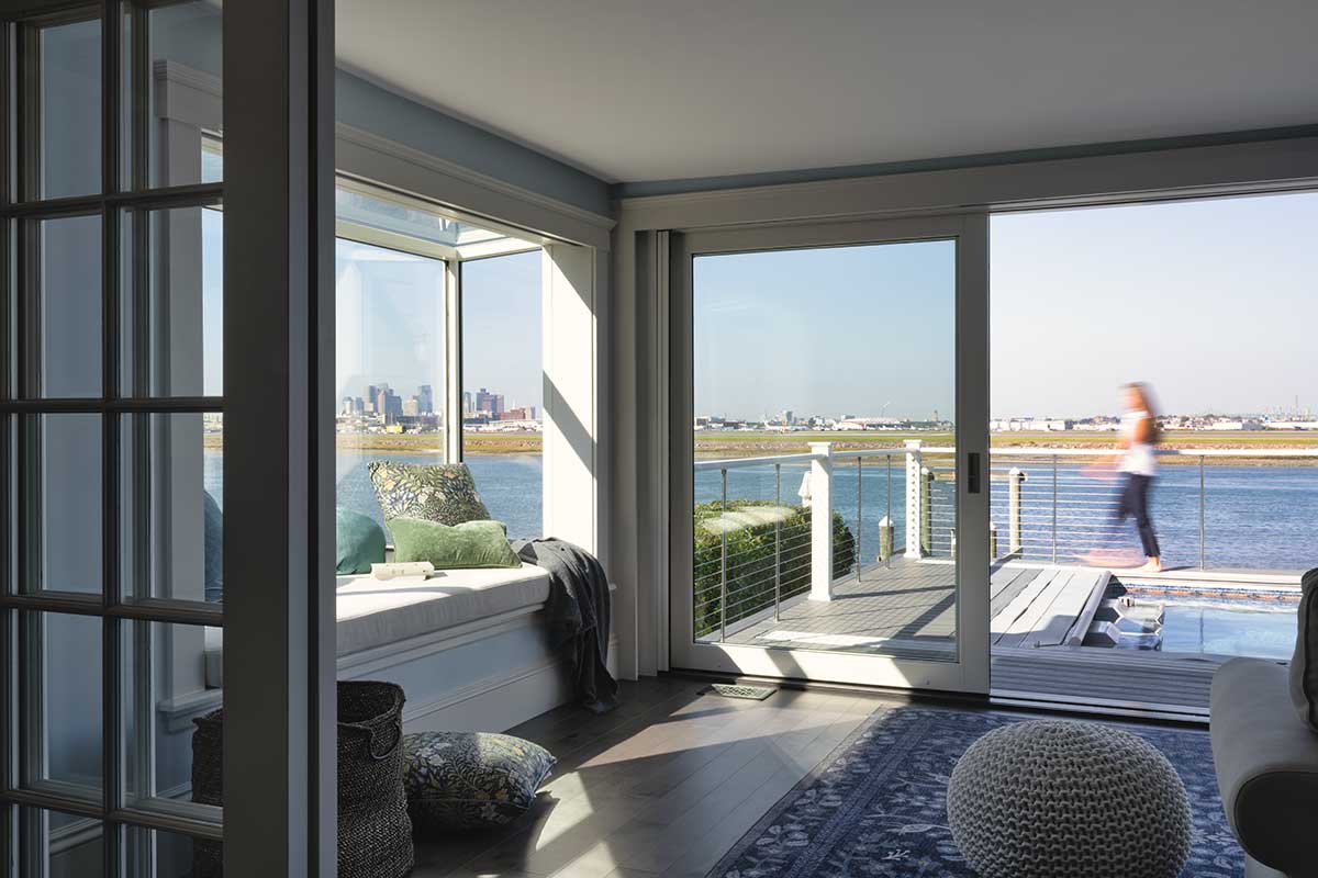 A living room featuring a Marvin Skycove and Ultimate Multi-Slide door leading out to a pool deck that overlooks a body of water.