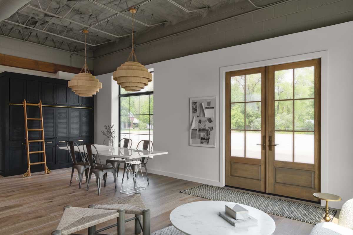 The interior of the Adorned Homes office space, with a seating area, conference table, dark cabinets with attached ladder and Marvin Essential Direct Glaze windows and an Ultimate Outswing French door G2.