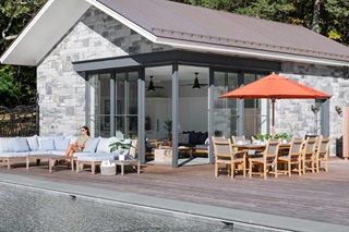 Woman lounges beside pool house featuring Marvin Ultimate Corner Multi-Slide door.