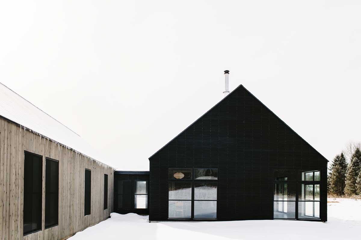 An exterior view from the side of Svart Hus in Door County, Wisconsin, showing two conjoined buildings. One with black-stained shiplap siding and the other with contrasting lighter stained wood.