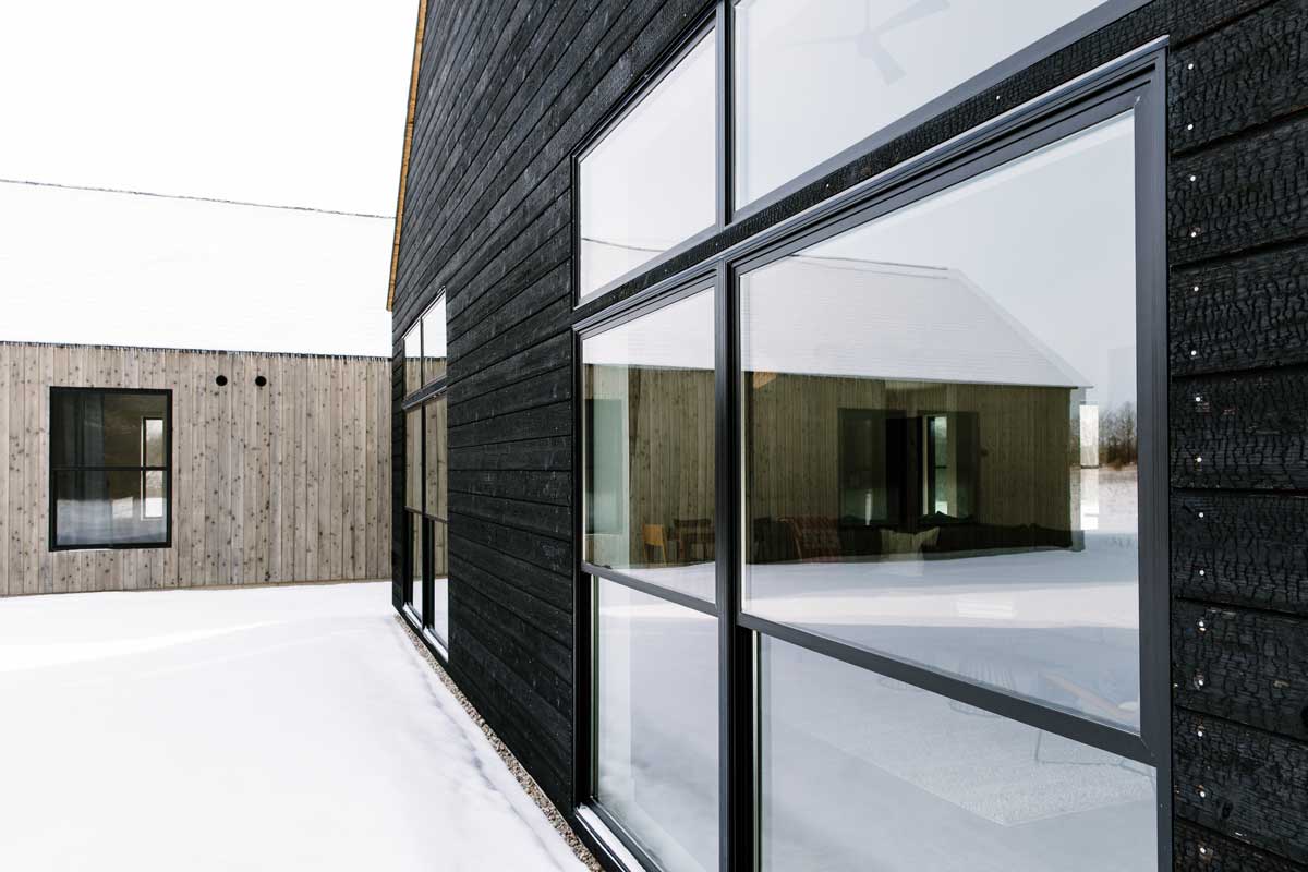 A side view of Svart Hus showing the detail of Marvin windows on coal black stained wood with the adjoined light natural wood building in the backgroud. 