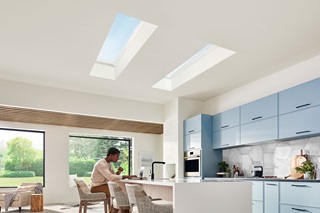A man working at a kitchen counter beneath two Marvin Awaken Skylights with two Marvin Skycoves behind him.